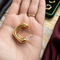 Gold hoop earring held in a hand with a jewelry box in the background