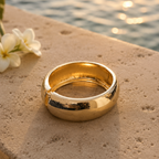 Gold ring on a sandy surface with water and flowers in the background