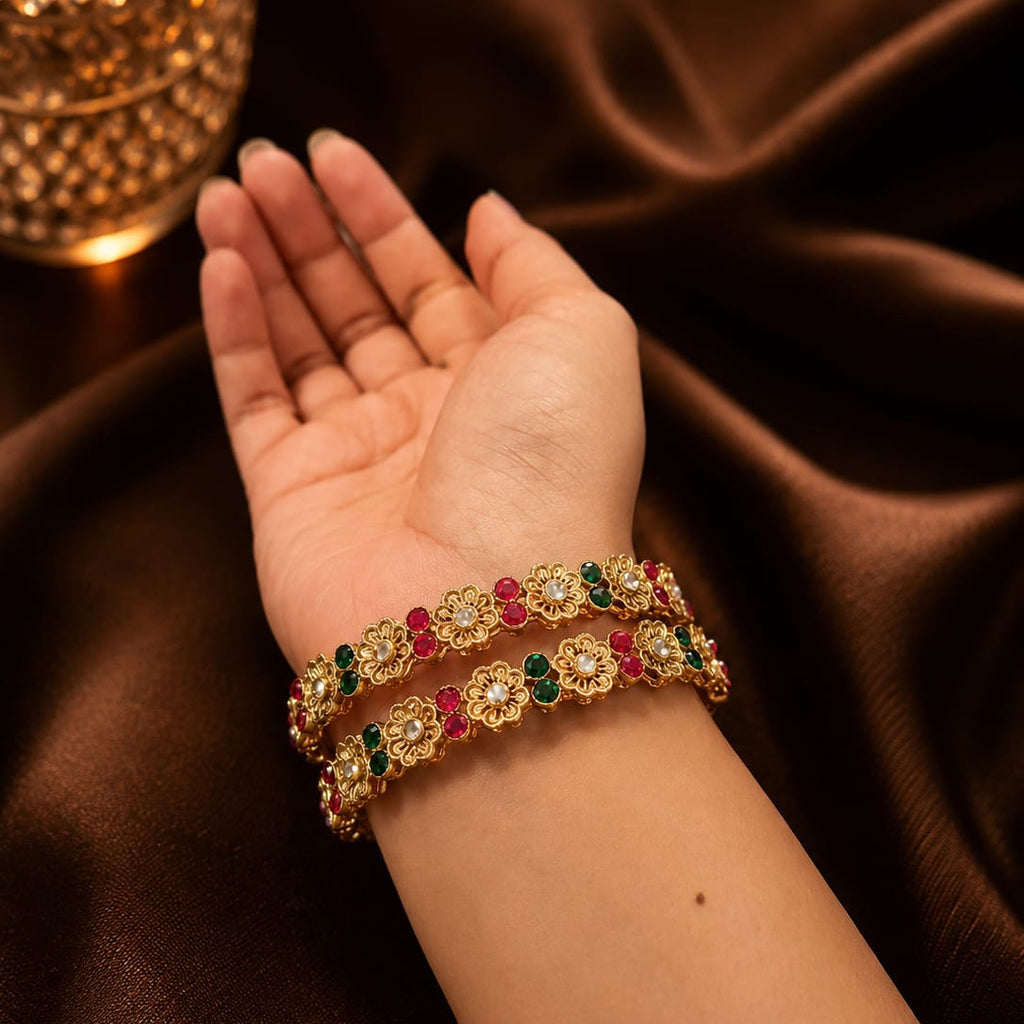 Gold bracelets with gemstones on a hand against a brown fabric background