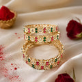 Gold ring with colorful gemstones on a white surface with red rose petals.
