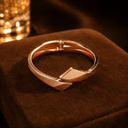 Rose gold bracelet on a brown textured surface with blurred lights in the background