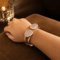 Close-up of a wrist wearing a gold bracelet with circular charms on a dark surface.