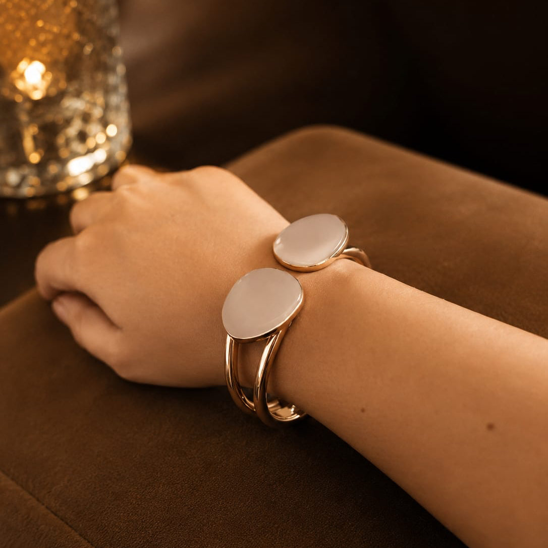 Close-up of a wrist wearing a gold bracelet with circular charms on a dark surface.