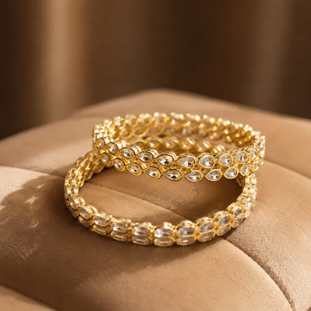 Gold beaded bracelet on a beige surface with a blurred brown background