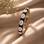Gold bracelet with white floral patterns on a beige surface