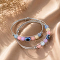 Stack of colorful beaded bracelets on a beige surface with dried flowers.