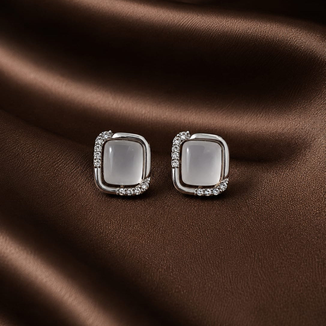 Pair of square-shaped earrings with a central gemstone on a brown fabric background