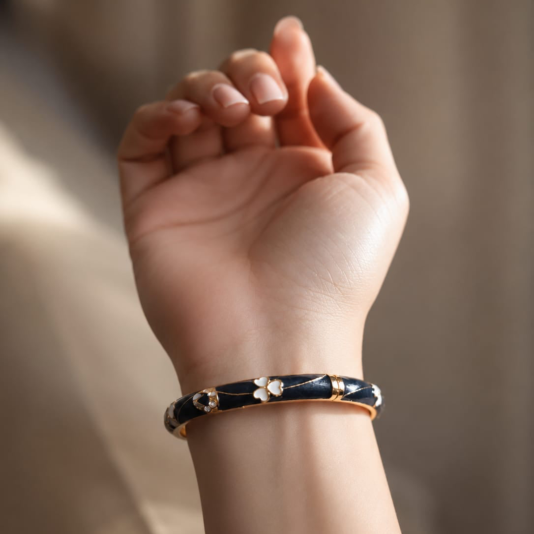 Hand wearing a black and gold bracelet against a neutral background