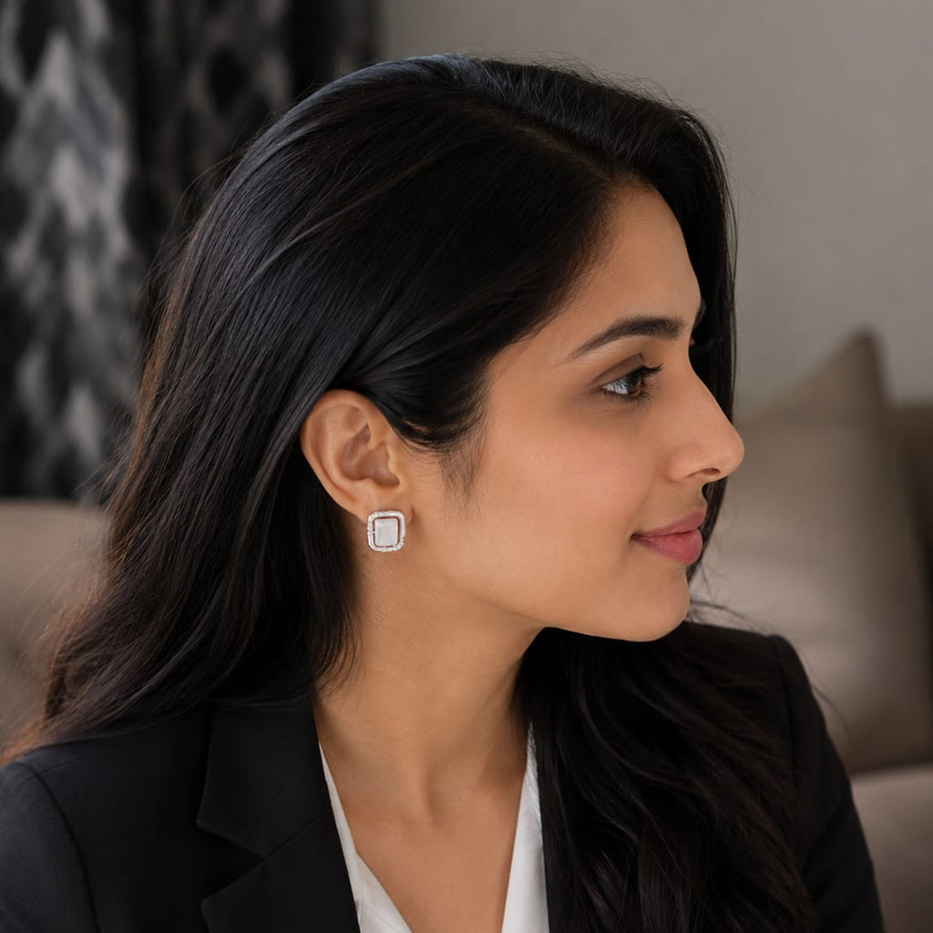 Woman wearing a black blazer and white shirt with earrings, sitting on a couch.
