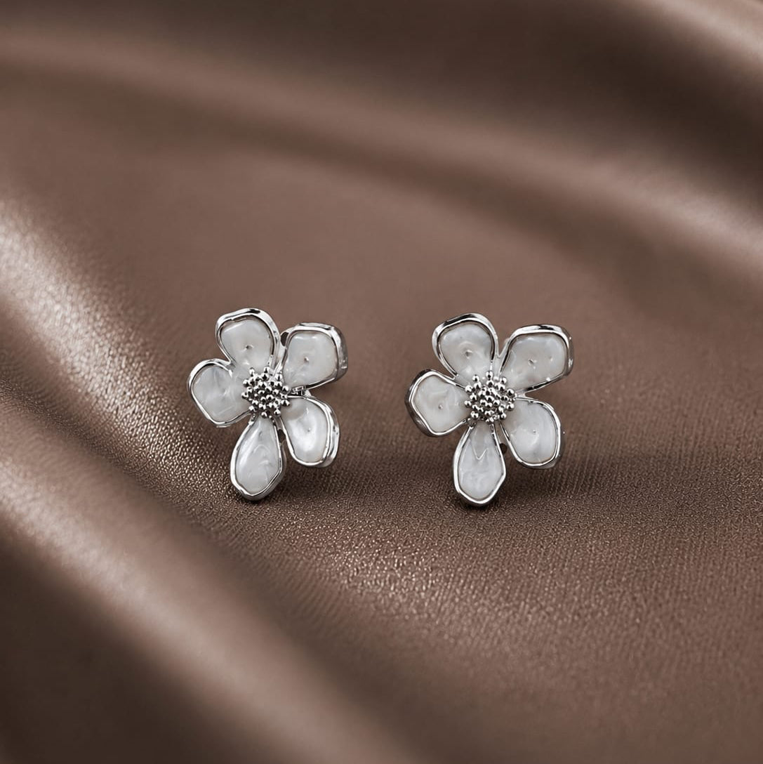 Flower-shaped silver earrings on a brown fabric background