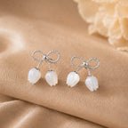 Silver earrings with bow and tulip design on a beige fabric background