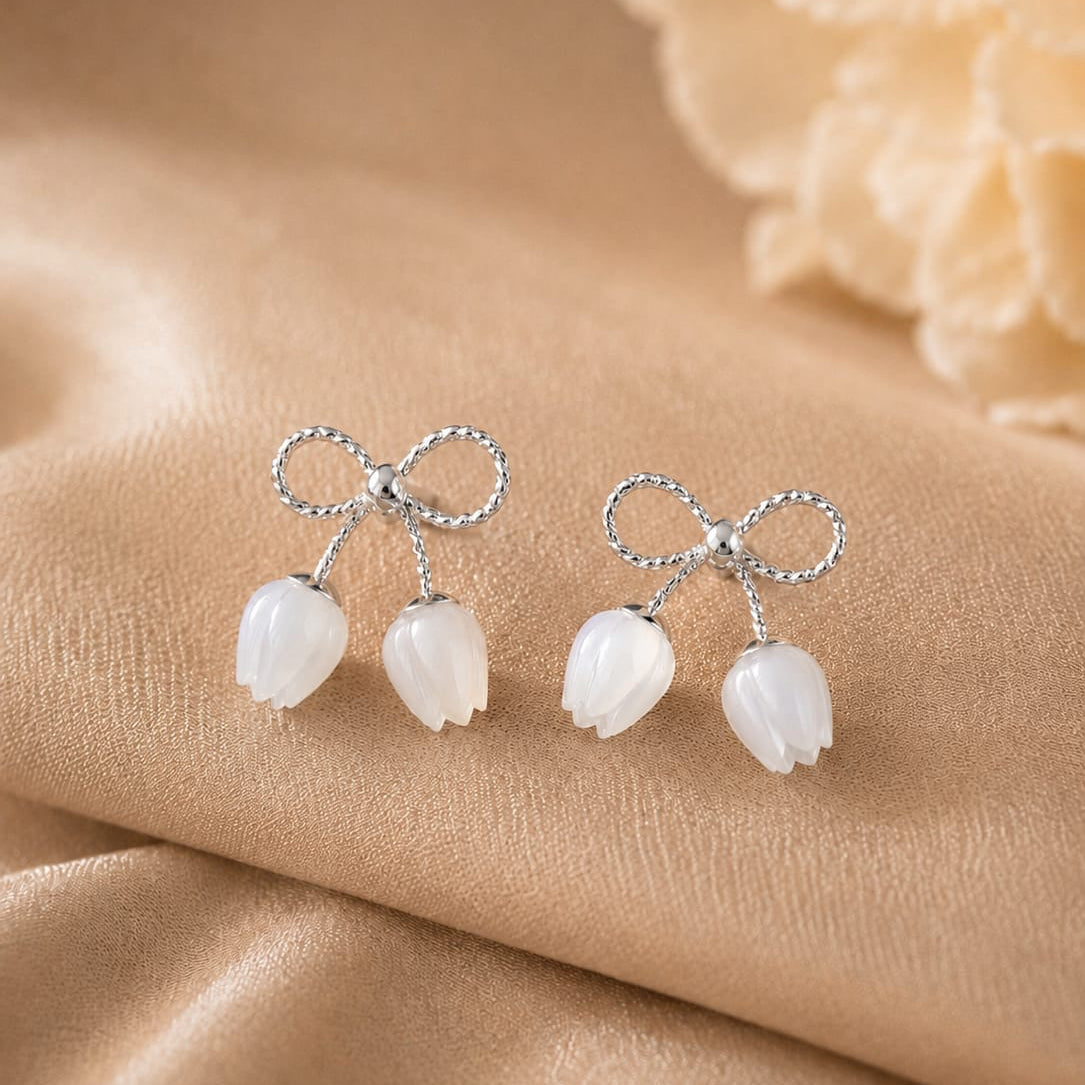 Silver earrings with bow and tulip design on a beige fabric background