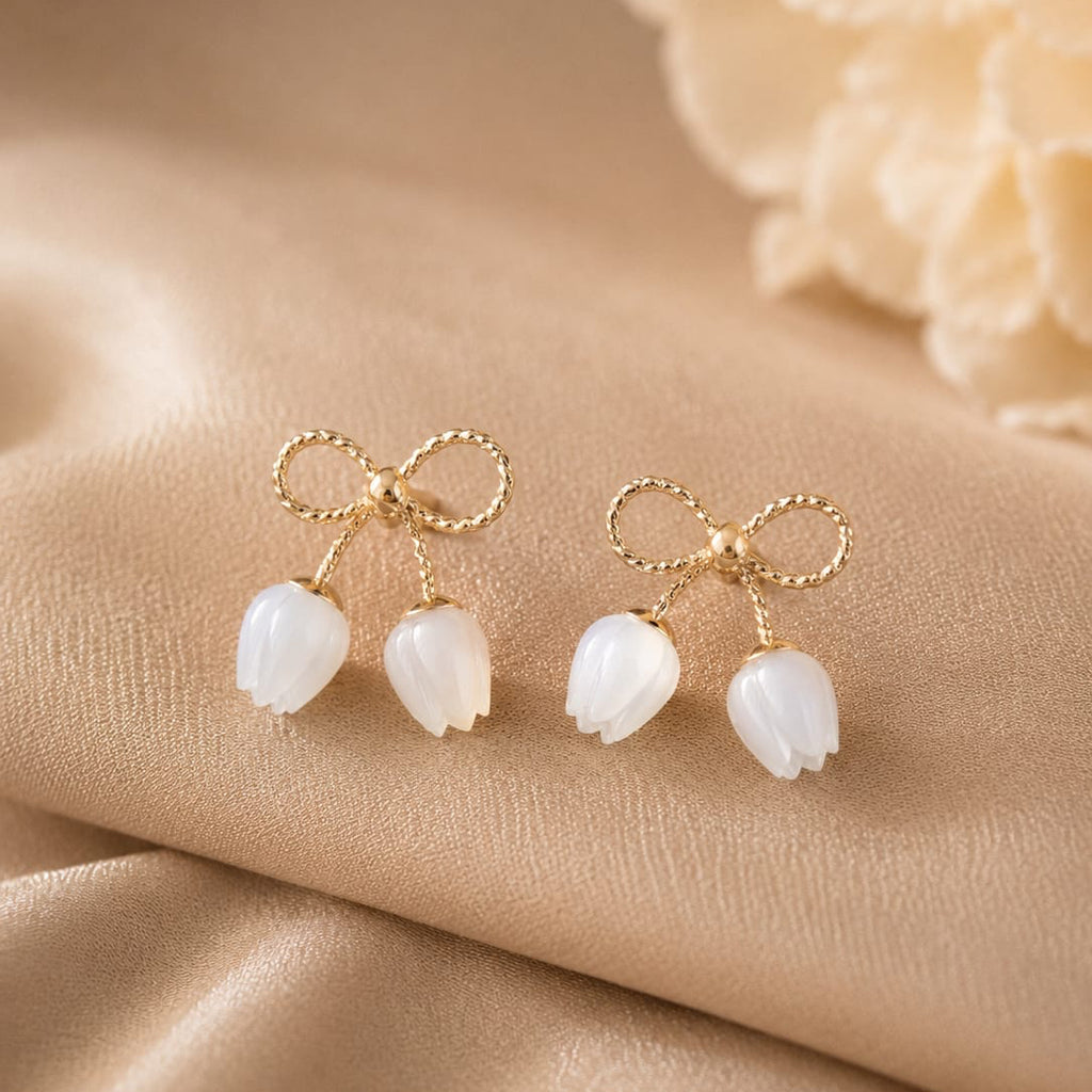 Gold bow and white tulip earrings on a beige fabric background