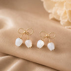 Gold bow and white tulip earrings on a beige fabric background