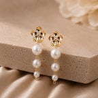 Gold earrings with pearl drops on a beige stone surface
