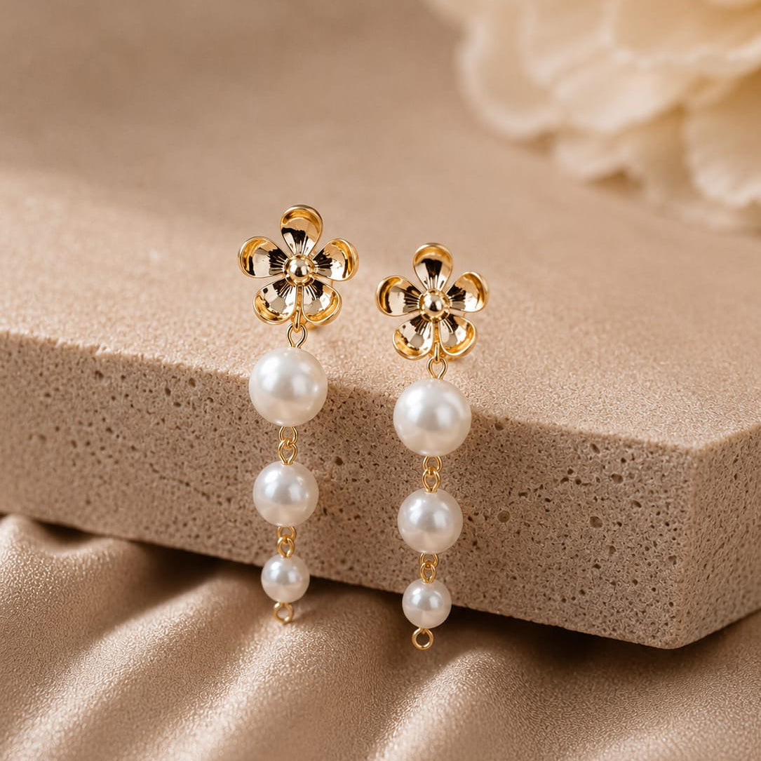 Gold earrings with pearl drops on a beige stone surface