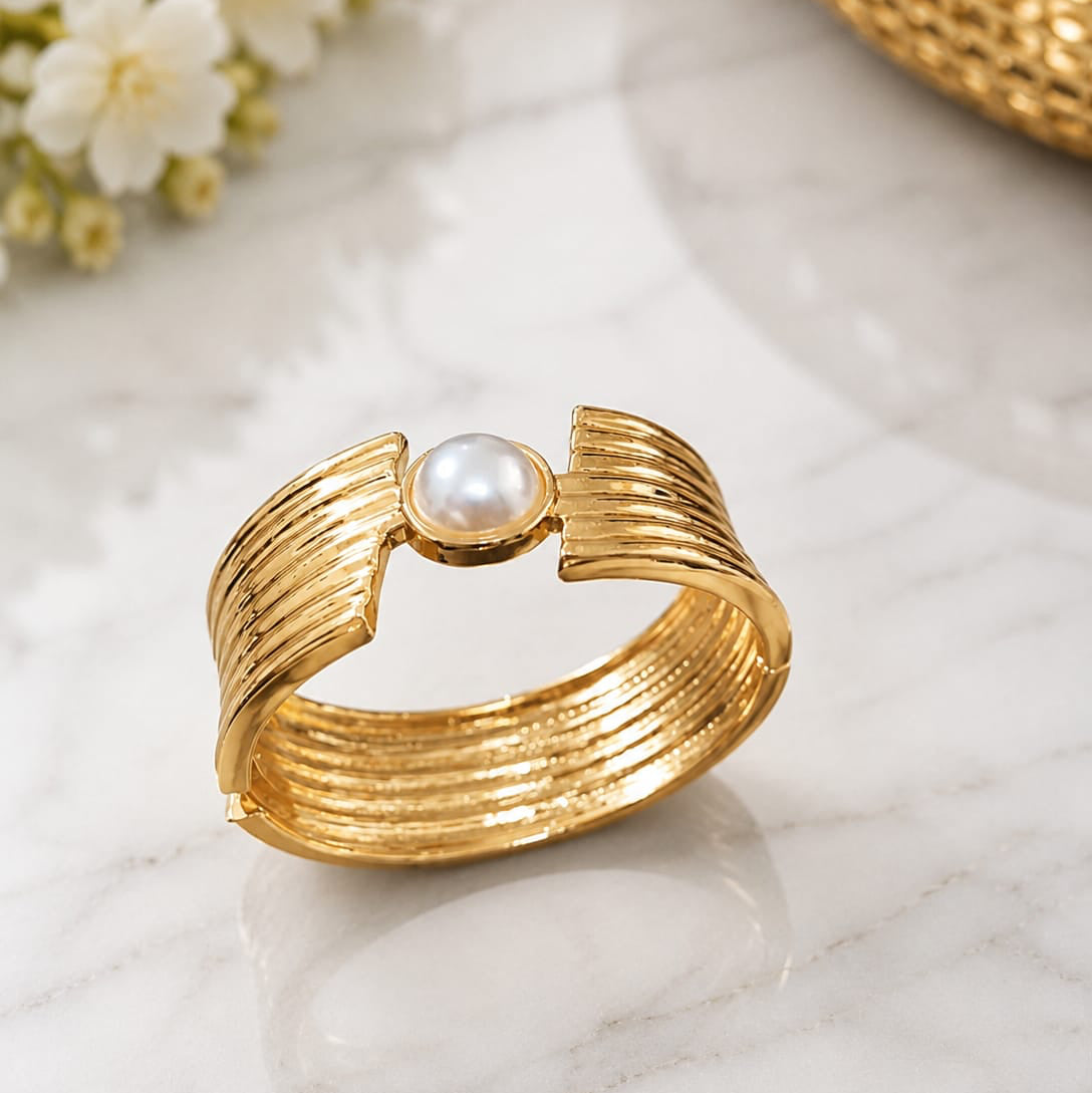 Gold ring with a pearl on a marble surface with flowers in the background