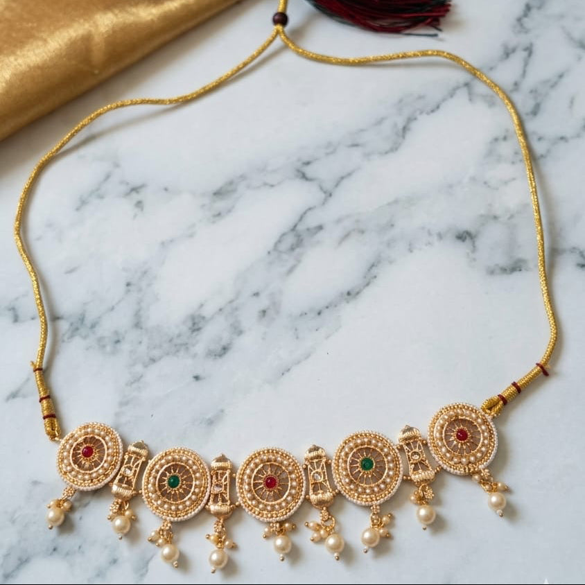 Gold necklace with red and gold fabric on a marble surface