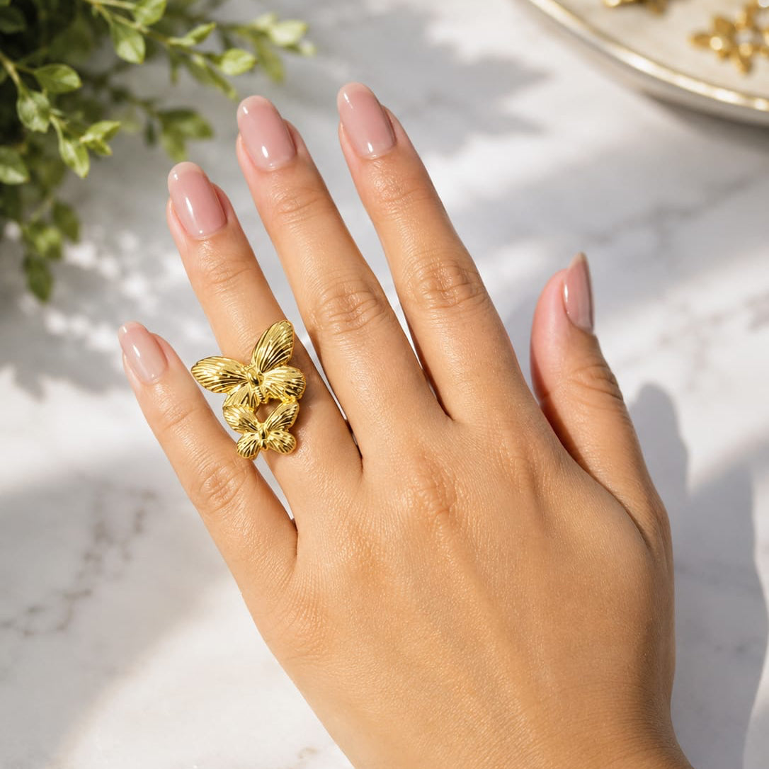 Hand wearing a gold ring with a decorative design on a marble surface.
