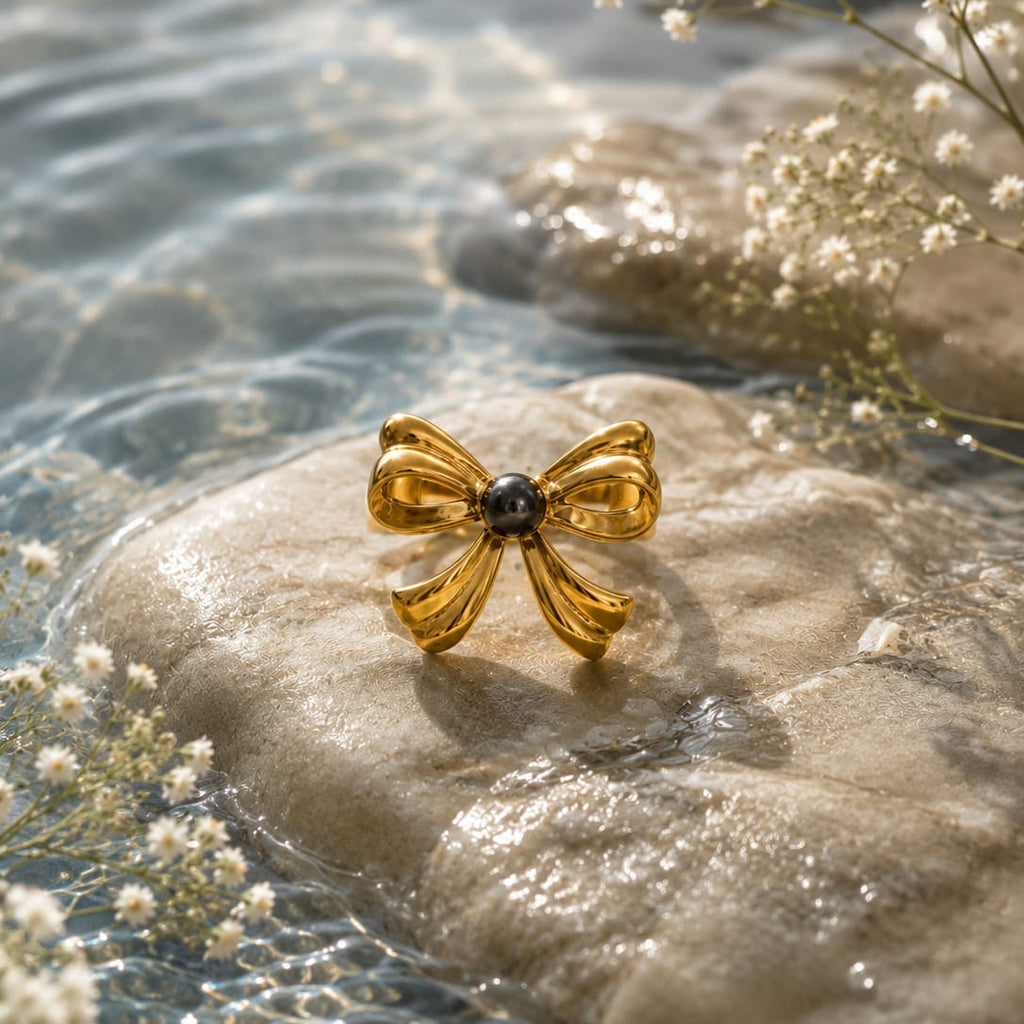 Gold bow-shaped ring with a black gemstone on a rock with water and flowers