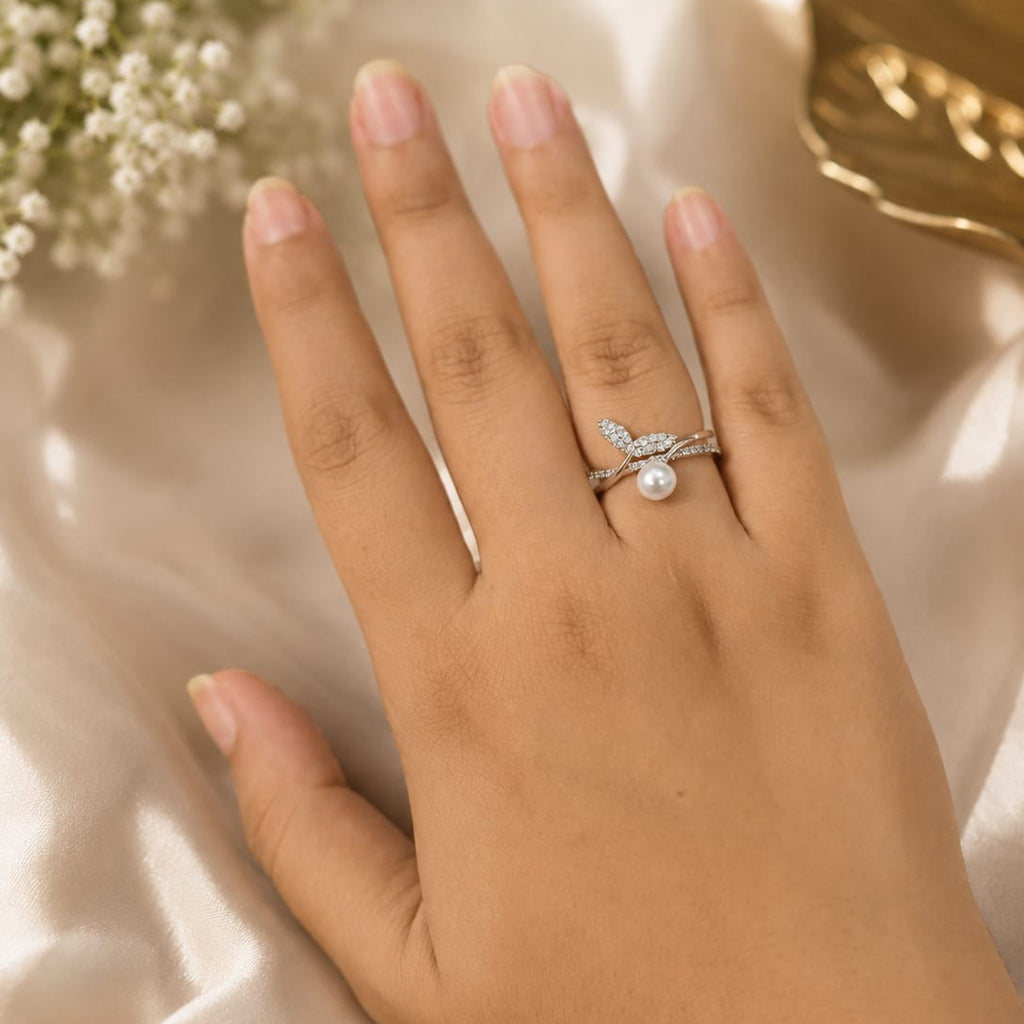 Hand wearing a ring with a pearl on a light background