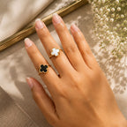 Hand wearing a gold ring with a black clover design on a neutral background