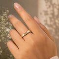 Hand wearing a gold ring with a white stone against a blurred natural background