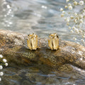 Gold earrings on a rock with water and flowers in the background