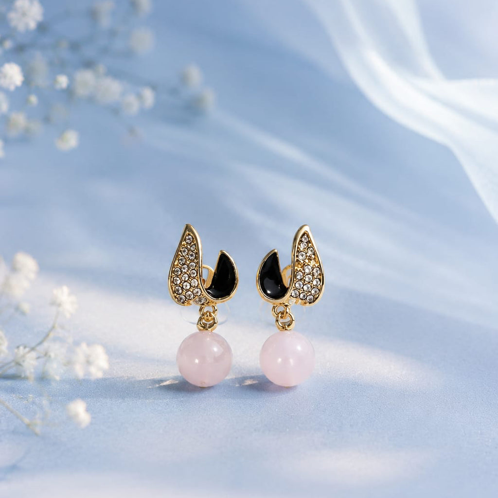 Pair of earrings with pink beads and gold and black accents on a soft blue background.