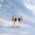 Pair of earrings with pink beads and gold and black accents on a soft blue background.