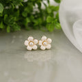 Pair of pearl flower earrings on a light surface with greenery in the background