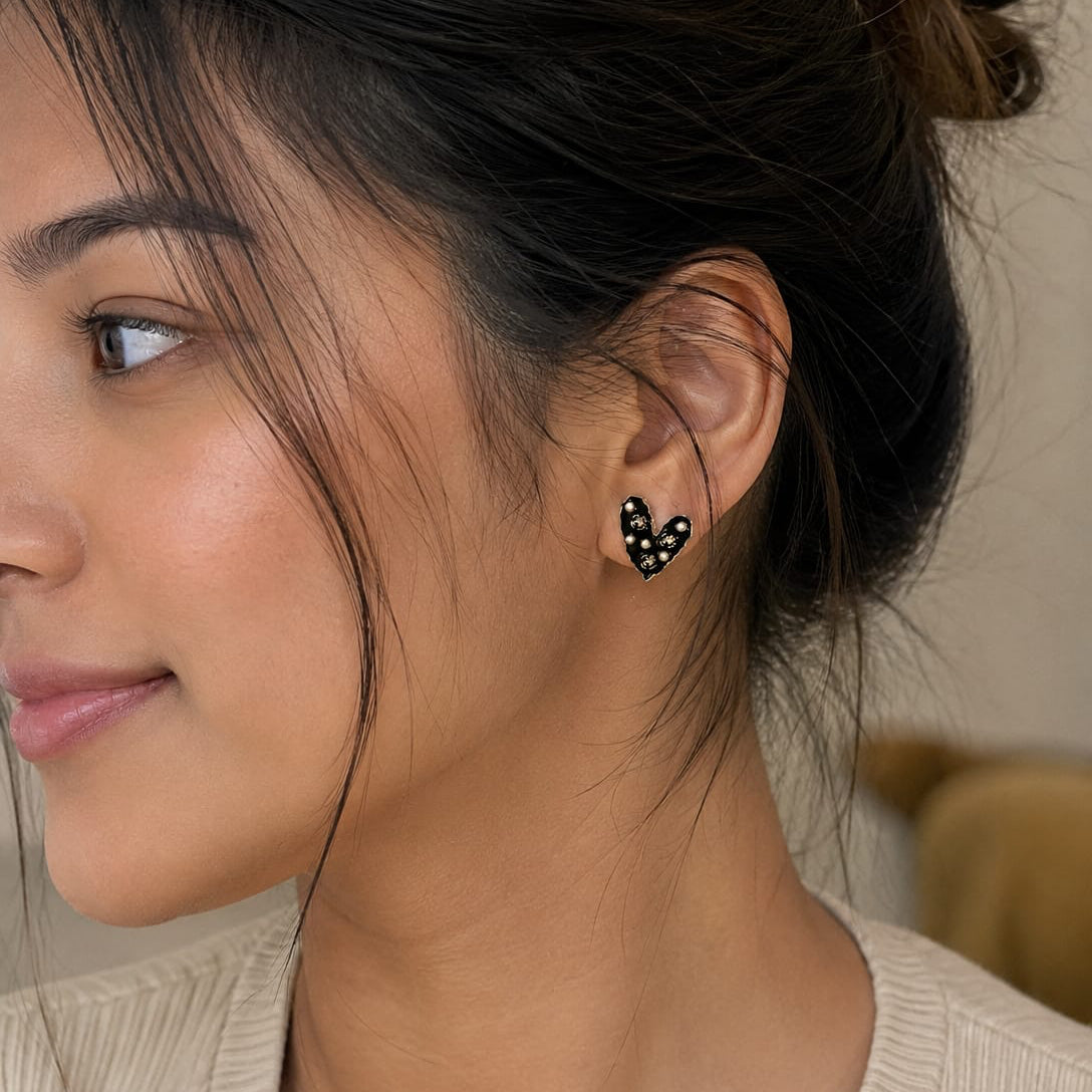 Close-up of a woman wearing black heart-shaped earrings with a neutral background