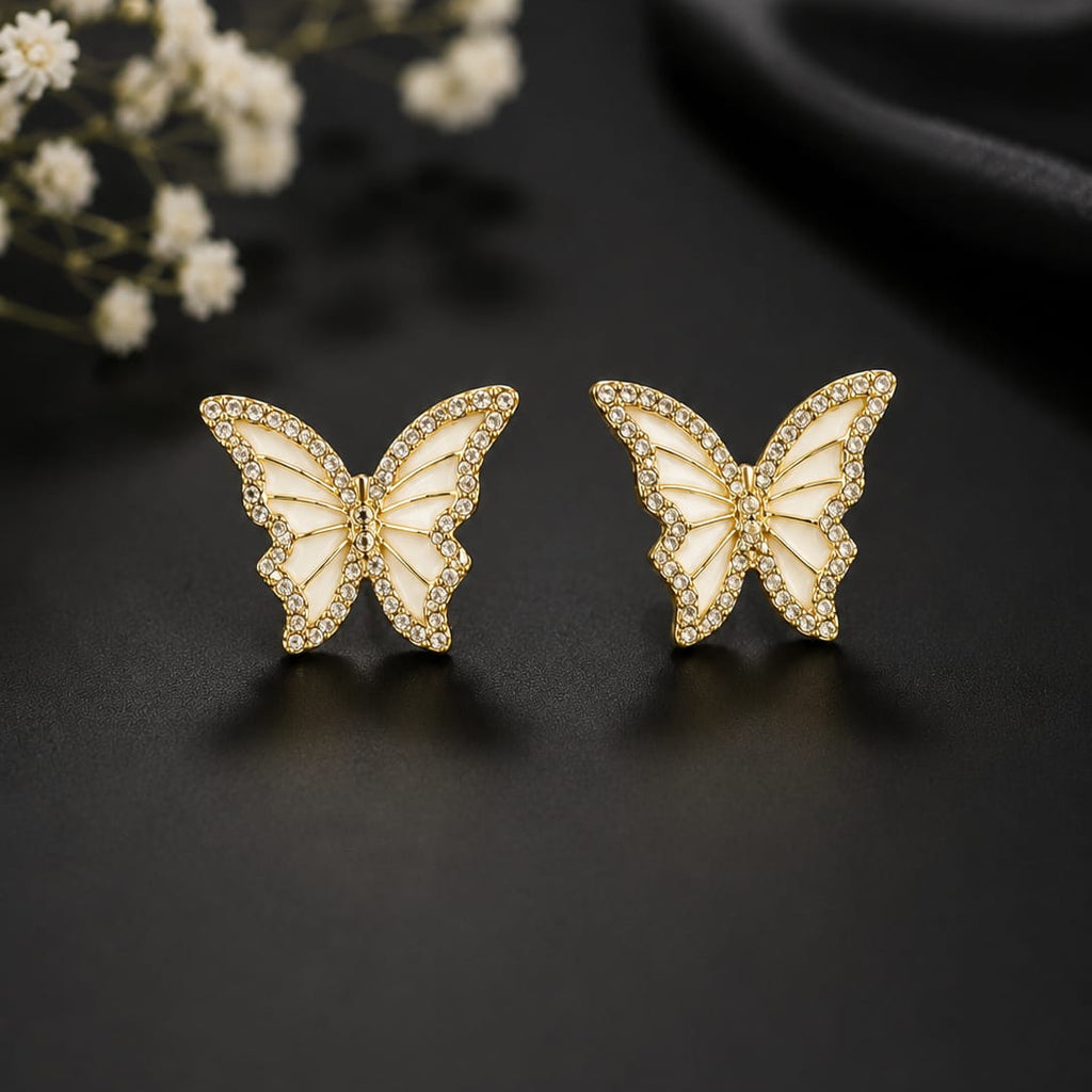 Butterfly-shaped earrings on a dark surface with white flowers in the background