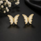 Butterfly-shaped earrings on a dark surface with white flowers in the background