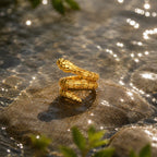 Gold ring on a rock with water and greenery in the background