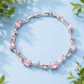 Silver bracelet with pink gemstones on a light blue background with green leaves.