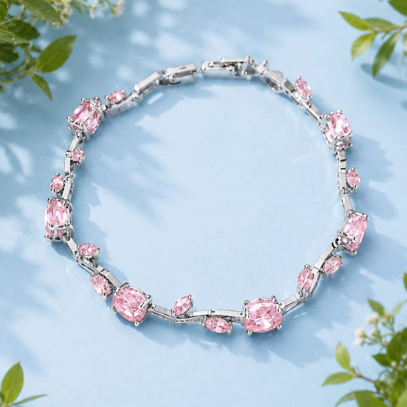 Silver bracelet with pink gemstones on a light blue background with green leaves.