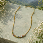 Gold necklace with colorful beads on a stone surface with a mountainous background