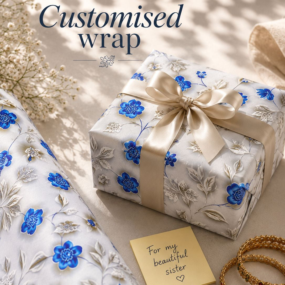 Gift wrapped in white paper with blue floral designs, gold ribbon, and a gold card on a light surface.