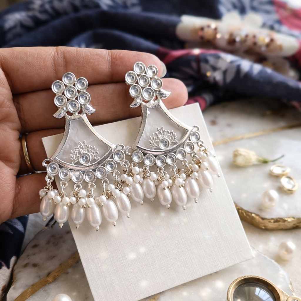 Silver earrings with pearls held by a hand on a marble surface.