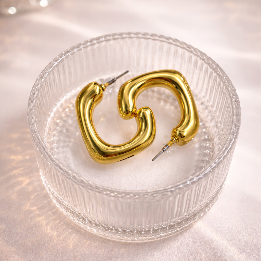 Gold hoop earrings on a textured glass dish with a soft light background