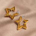 Gold star-shaped earrings on a beige fabric background