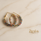 Colorful beaded hoop earrings on a marble surface with 'Zeraya' branding.