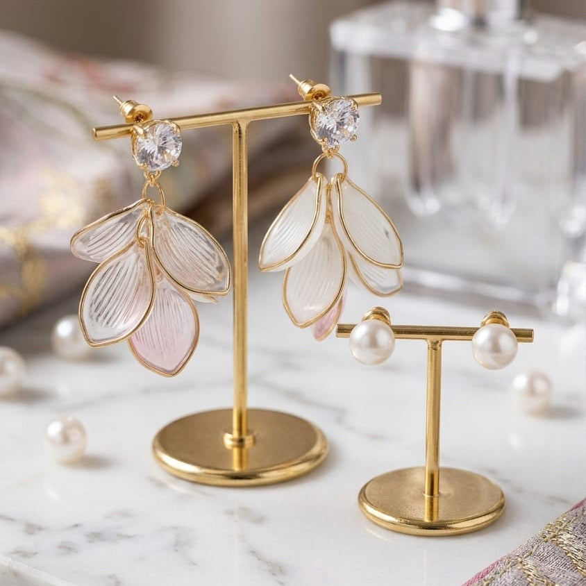Gold earring stand with floral earrings on a marble surface next to a perfume bottle.