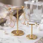 Gold earring stand with floral earrings on a marble surface next to a perfume bottle.