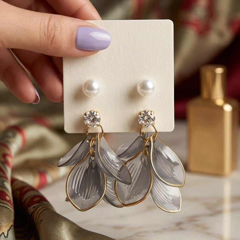 Hand holding a pair of earrings on a display card with a patterned fabric background